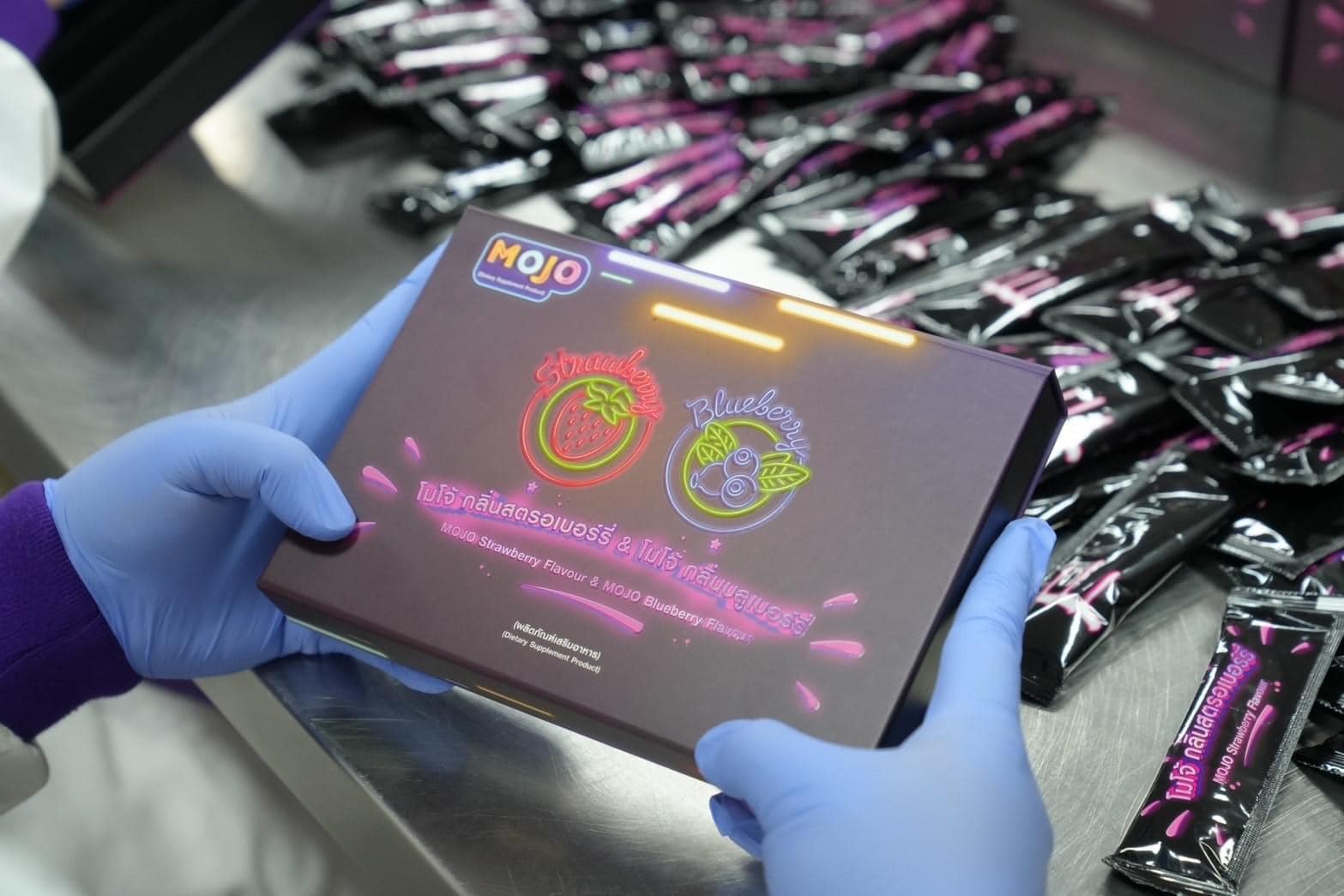 Person holding a 'MOJO' product box with gloves on, surrounded by similar products.